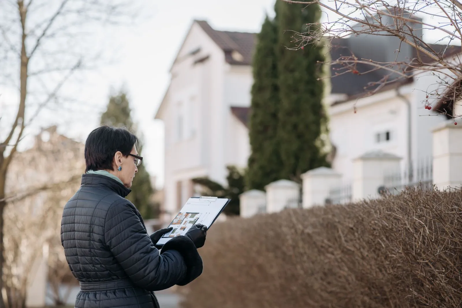 An appraiser in business-casual clothes with a clipboard looking over a house from the street